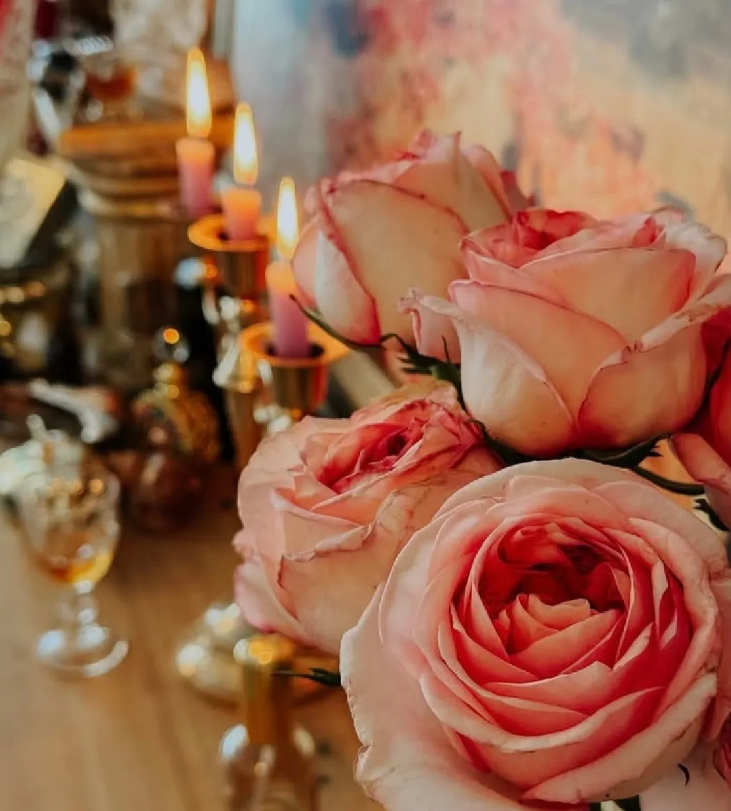 Rosas cor-de-rosa em primeiro plano, com velas acesas e frascos ao fundo.